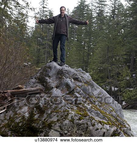 Picture - Man standing with his arm outstretched on a rock at the riverside, Nairn Falls Provincial Park, Whistler, British Columbia, Canada. Fotosearch