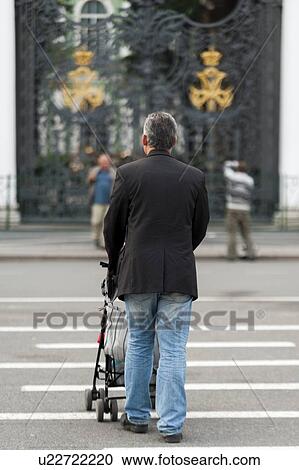 Stock Image - Man walking with a pram towards State Hermitage Museum, Palace Square, St. Petersburg, Russia. Fotosearch