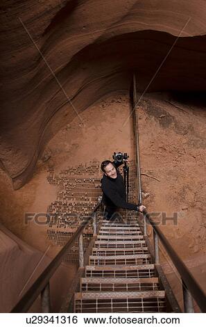 Stock Photograph - Photographer moving up staircase in a slot canyon, Corkscrew Canyon, Lower Antelope Canyon, Antelope Canyon, Page, Arizona, USA. Fotosearch