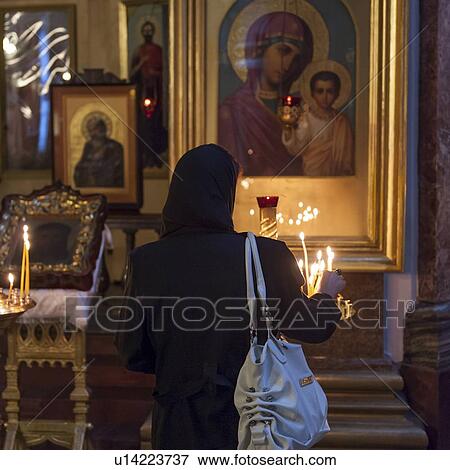 Stock Photo - Rear view of a woman lighting candles in the Cathedral of Our Lady of Kazan, St. Petersburg, Russia. Fotosearch