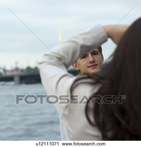 Stock Image - Rear view of a woman taking a picture of his boyfriend at the riverside, St. Petersburg, Russia. Fotosearch