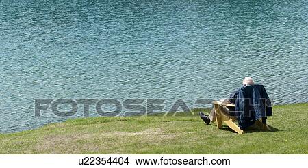 Picture - Senior man sitting on a chair at the lakeside, Beauvert Lake, Jasper National Park, Alberta, Canada. Fotosearch