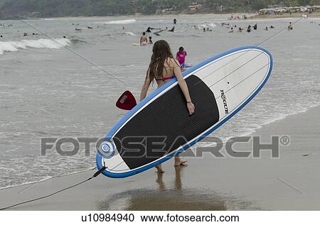 Stock Image - Woman carrying a surfboard on the beach, Sayulita, Nayarit, Mexico. Fotosearch