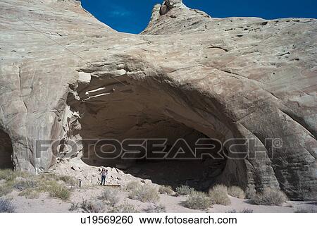 Stock Image - Woman standing at the entrance of Ulrike's Cave, Amangiri, Canyon Point, Utah, USA. Fotosearch