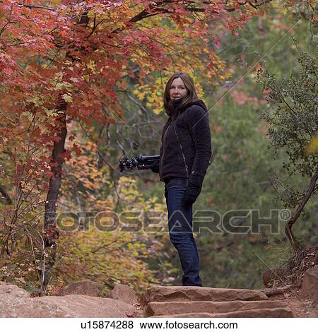 Stock Photo - Woman standing with a tripod in a forest, Zion National Park, Utah, USA. Fotosearch