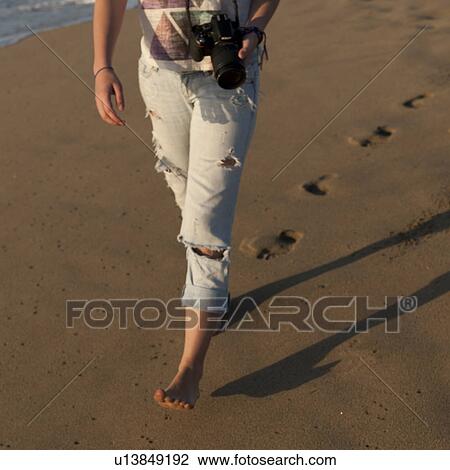 Stock Image - Woman walking with a digital camera on the beach, Sayulita, Nayarit, Mexico. Fotosearch
