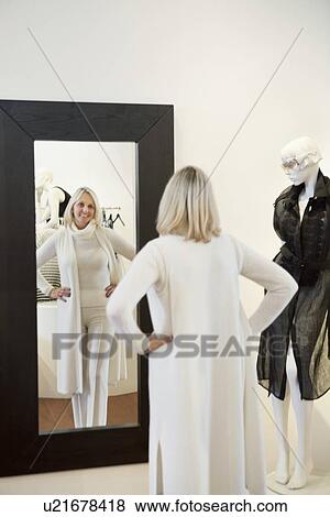 Stock Photo - Back view of a senior woman standing with hands on hips in front of mirror looking at herself. Fotosearch