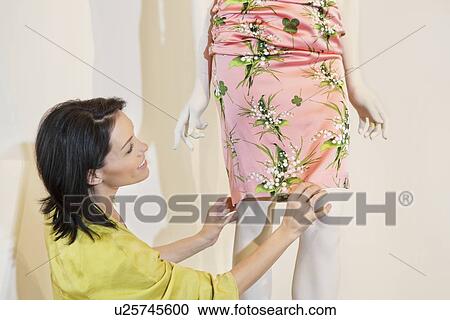 Stock Image - Beautiful mid adult woman adjusting dress on mannequin in fashion store. Fotosearch