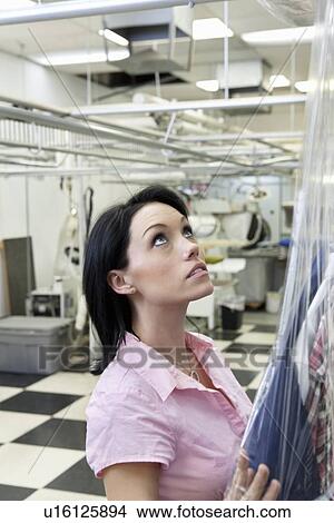Beautiful mid adult woman putting plastic to dry cleaned while looking up View Large Photo Image Picture - Beautiful mid adult woman putting plastic to dry cleaned while looking up. Fotosearch