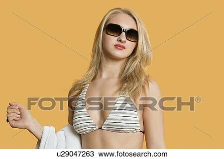 Stock Image - Beautiful young woman in bikini with towel in hand over colored background. Fotosearch