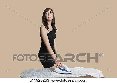 Beautiful young woman looking up while ironing shirt over colored background View Large Photo Image Stock Image - Beautiful young woman looking up while ironing shirt over colored background. Fotosearch