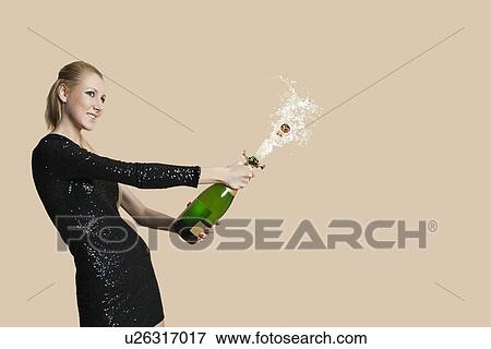 Beautiful young woman uncorking champagne bottle over colored background View Large Photo Image Stock Photo - Beautiful young woman uncorking champagne bottle over colored background. Fotosearch