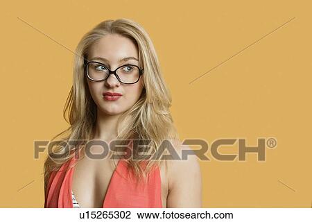 Stock Image - Beautiful young woman wearing retro glasses looking away over colored background. Fotosearch