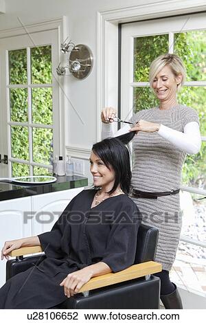 Stock Image - Cheerful hairstylist giving a haircut to beautiful mid adult woman in beauty salon. Fotosearch