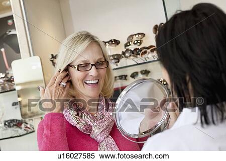 Cheerful senior woman trying on glasses while optician holding mirror View Large Photo Image Stock Photography - Cheerful senior woman trying on glasses while optician holding mirror. Fotosearch