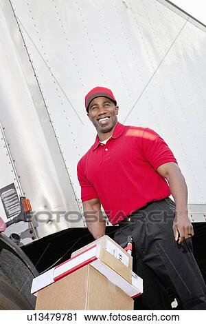 Stock Image - Cheerful young delivery person pushing handtruck. Fotosearch