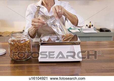 Stock Image - Close-up of a female employee measuring spice on weight scale in store. Fotosearch