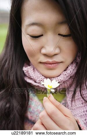 Stock Image - Close-up of a young Asian woman looking at flower. Fotosearch