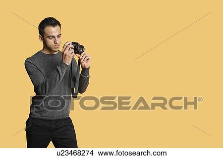 confident young man with digital camera over colored background View Large Photo Image Picture - confident young man with digital camera over colored background. Fotosearch