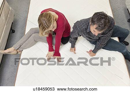 Stock Image - Friends sitting on mattress in furniture store. Fotosearch