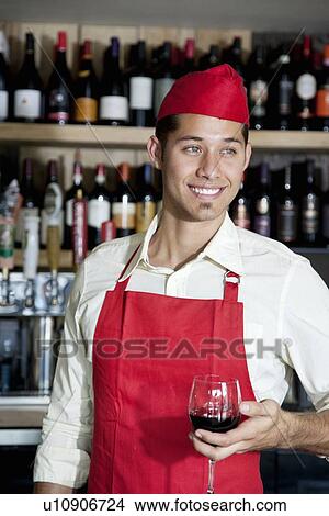 Picture - Happy handsome bartender holding glass of wine in bar. Fotosearch