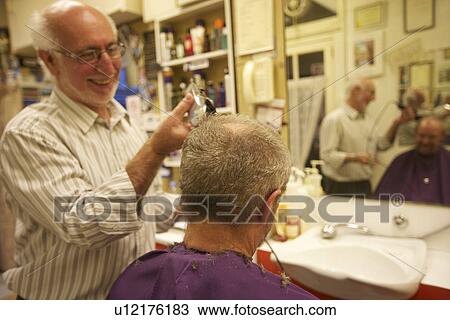 Stock Image - Happy man cutting senior customer's hair with razor. Fotosearch