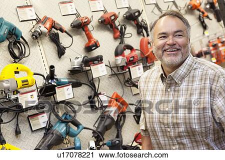 Stock Image - Happy mature hardware store owner looking away. Fotosearch
