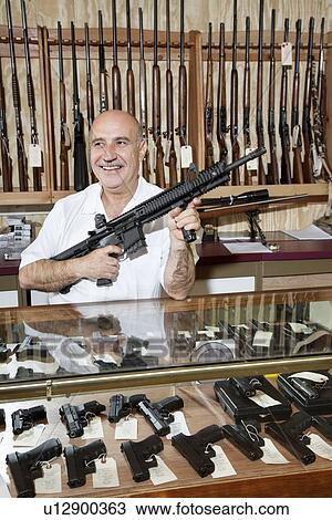 Stock Image - Happy mature man with rifle in gun store. Fotosearch