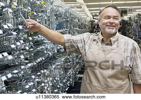 Stock Photography - Happy mature salesperson holding metallic equipment while looking away in hardware store. Fotosearch