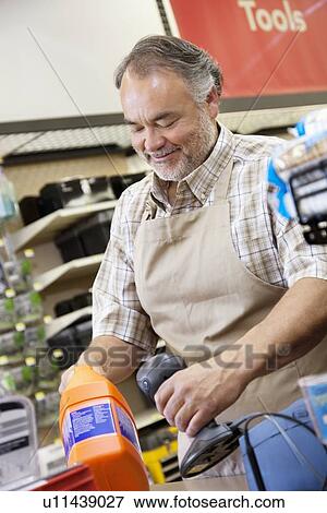 Stock Photo - Happy mature salesperson using barcode reader at checkout counter in hardware counter. Fotosearch