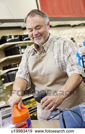 Stock Photo - Happy mature store clerk using barcode reader at checkout counter. Fotosearch