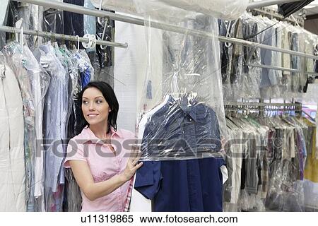 Stock Photography - Happy mid adult woman looking away while putting clothes in plastic. Fotosearch