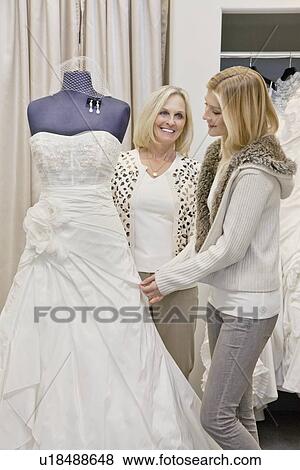 Stock Photo - Happy mother and daughter looking at beautiful wedding dress in bridal store. Fotosearch