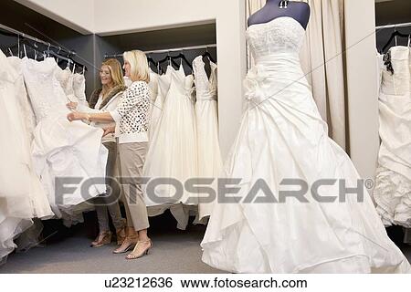 Stock Photograph - Happy mother and daughter shopping together for wedding gown in boutique. Fotosearch