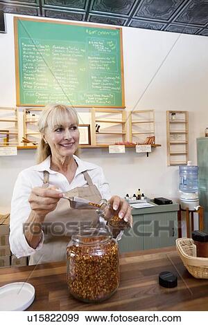 Happy senior female filling jar with scoop while looking away in store View Large Photo Image Stock Photo - Happy senior female filling jar with scoop while looking away in store. Fotosearch