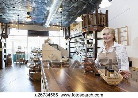 Stock Photography - Happy senior female spice merchant standing at counter while looking away in store. Fotosearch