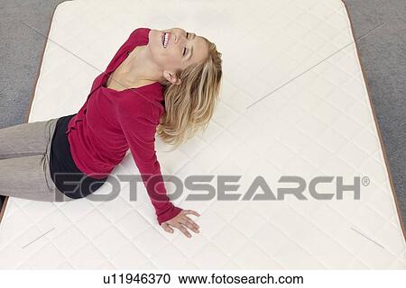 Stock Image - Happy woman relaxing on mattress with head back in furniture store. Fotosearch
