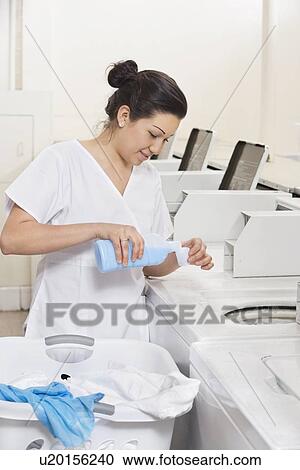 Stock Image - Happy young female employee pouring detergent in washing machine Laundromat. Fotosearch