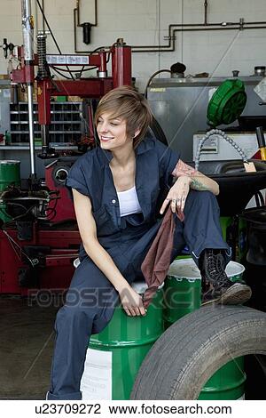Happy young female mechanic sitting on oil drum in automobile repair shop View Large Photo Image Stock Image - Happy young female mechanic sitting on oil drum in automobile repair shop. Fotosearch