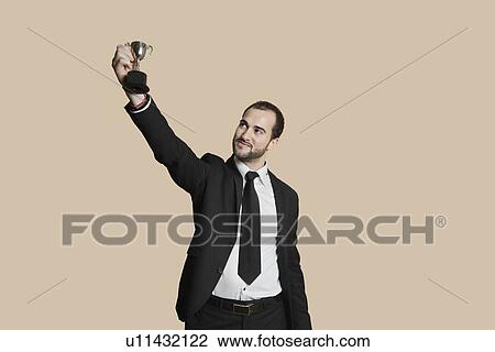 Stock Image - Happy young man raising winning trophy over colored background. Fotosearch
