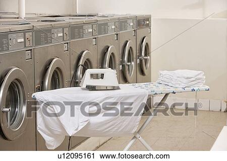 Stock Image - Ironing board with washing machines in Laundromat. Fotosearch