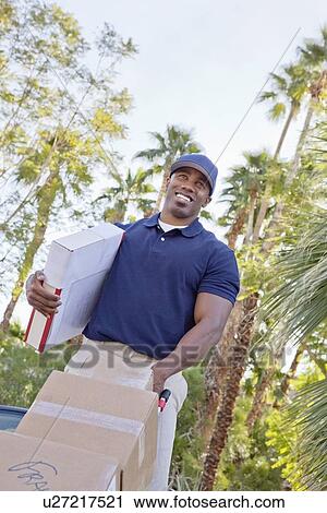 Stock Image - Low angle view of a happy delivery male with packages. Fotosearch