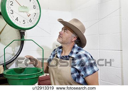 Stock Photo - Mature cowboy looking up at weight scale. Fotosearch