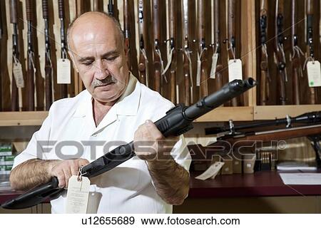 Mature gun shop merchant looking at rifle in store View Large Photo Image Stock Photo - Mature gun shop merchant looking at rifle in store. Fotosearch