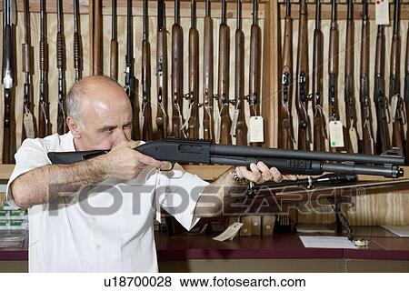 Stock Photo - Mature gun shop merchant with rifle aiming. Fotosearch