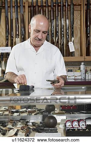 Stock Image - Mature male merchant at gun shop with credit card reader. Fotosearch