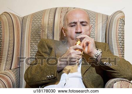 Mature man igniting cigar while sitting on armchair View Large Photo Image Stock Image - Mature man igniting cigar while sitting on armchair. Fotosearch