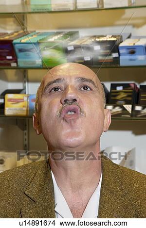Picture - Mature man in tobacco store blowing smoke. Fotosearch