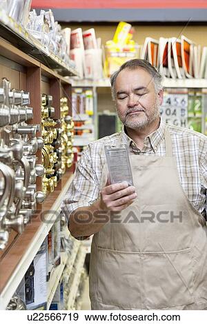 Stock Photo - Mature salesperson reading instructions in hardware store. Fotosearch