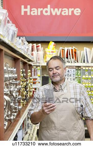 Stock Image - Mature salesperson reading something in hardware store. Fotosearch